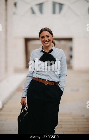 Una donna d'affari latina sorridente si muove con sicurezza per le strade urbane. Foto Stock