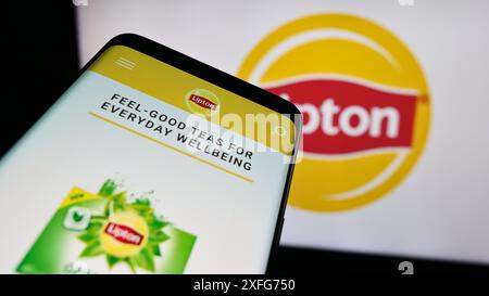 Telefono cellulare con sito web del marchio Tea Lipton davanti al logo aziendale. Mettere a fuoco in alto a sinistra sul display del telefono. Foto Stock