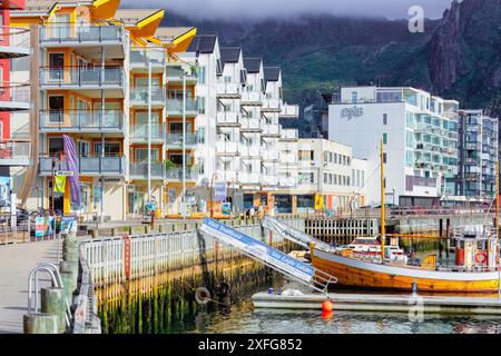 Sul lungomare di Svolvær, con edifici e barche moderni e colorati, montagne nebbiose sullo sfondo. Concetto di viaggio per destinazioni fredde alla moda. Foto Stock