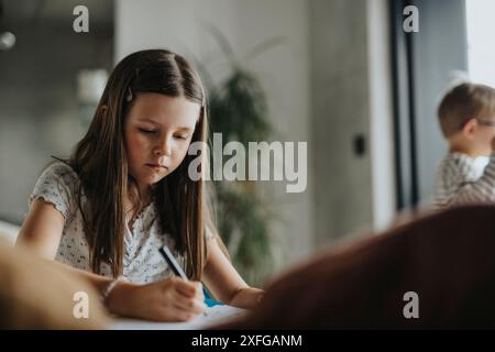 Ragazza concentrata che scrive nel libro a casa Foto Stock