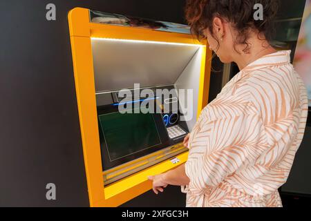 Donna latina ispanica che usa il bancomat durante il giorno. Vista posteriore. Foto Stock