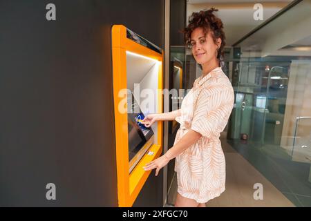 Donna latina ispanica che usa il bancomat durante il giorno. Sta guardando la macchina fotografica e sorride. Foto Stock