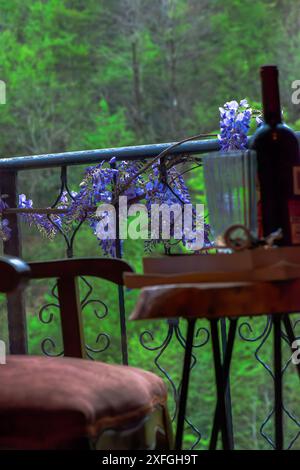 Un ambiente sereno con una bottiglia di vino su una scrivania, completata dalla bellezza dei fiori di Wisteria in un ambiente naturale. Foto Stock