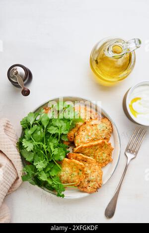 Frittelle di zucchine vegetali con panna acida pepe e olio d'oliva servite su un piatto rustico su un vecchio sfondo di piastrelle incrinate. Vegetariano sano per Foto Stock