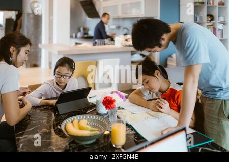 I bambini studiano con la madre mentre sono seduti a tavola in casa Foto Stock