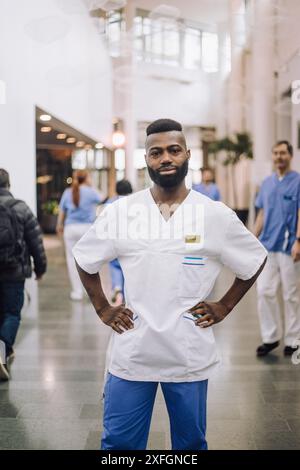 Ritratto di infermiera maschio fiducioso in piedi con le braccia akimbo nella hall dell'ospedale Foto Stock