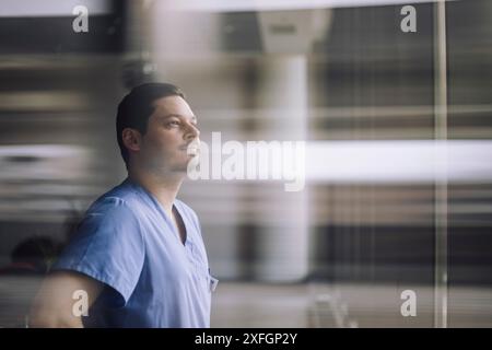 Medico maschio maturo guardando attraverso la finestra di vetro all'ospedale Foto Stock