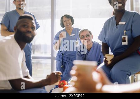 Medici sorridenti maschili e femminili durante la pausa caffè in mensa ospedaliera Foto Stock