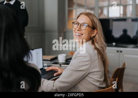 Donna d'affari felice che indossa gli occhiali da vista seduta in ufficio Foto Stock