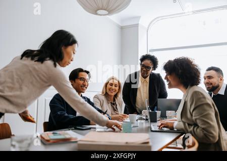 Donna d'affari che fissa appunti adesivi sulla scrivania nella sala riunioni con i colleghi in ufficio Foto Stock