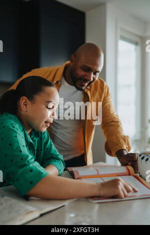 Padre felice che aiuta la figlia a leggere dal libro di testo a casa Foto Stock