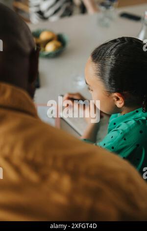 Vista a spalla del padre che assiste la figlia negli studi a casa Foto Stock