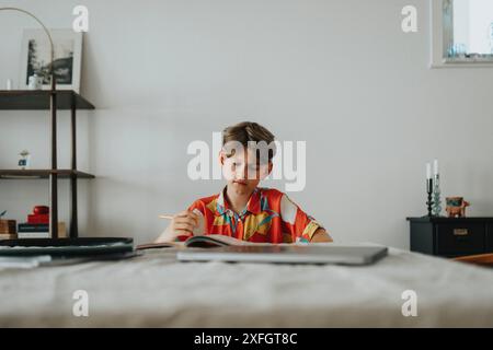 Ragazzo che fa i compiti mentre siede vicino a un tavolo a casa Foto Stock