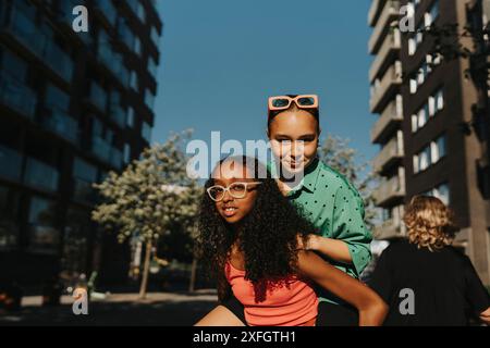 Una ragazza adolescente che fa il piggyback con un amico mentre cammina per strada Foto Stock