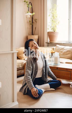 Giovane donna che pratica yoga seduto a gambe incrociate nel soggiorno di casa Foto Stock