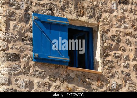 Finestra con persiane in legno blu su una parete in pietra, persiane scure Foto Stock