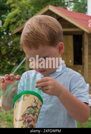 Ritratto di un bambino. Apre un cono di caramelle con interesse. Gioia, curiosità, scuola. Foto Stock