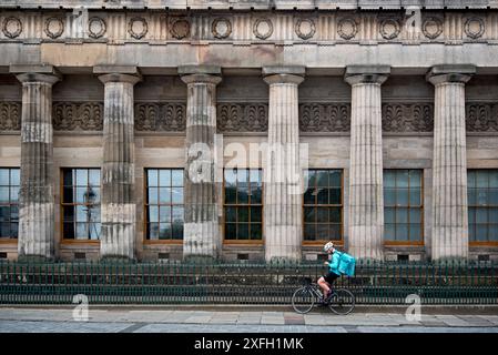 Il corriere Deliveroo si prende una pausa al lato dell'edificio della Royal Scottish Academy sul Mound, Edimburgo, Scozia, Regno Unito. Foto Stock