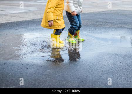 Due bambini con stivali antipioggia si tuffano in una pozzanghera dopo un temporale. Foto Stock