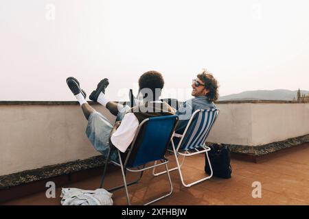 Amici maschi felici che trascorrono del tempo libero seduti sulle sedie sul tetto Foto Stock
