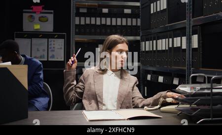 Sul telefono fisso, una donna delle forze dell'ordine riceve informazioni critiche e fornisce nuovi indizi sui casi alla poliziotta afroamericana. Nella sala degli incidenti, investigatore privato caucasico su chiamata. Foto Stock