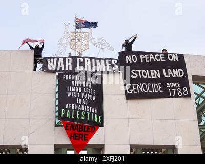 4 luglio 2024, Australia, Canberra, Parlamento. Manifestante pro-Palestina scalare il tetto della camera del Parlamento australiana per svelare striscioni che criticano il ruolo del governo australiano nell'agevolare il genocidio a Gaza Foto Stock