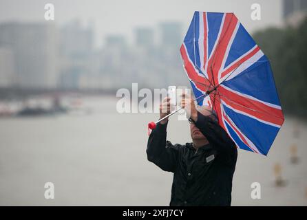 Foto datata 13/08/15 di un ombrello di un uomo che esplode dentro mentre scatta una foto con il suo cellulare a Westminster, Londra. Venti fino a 40 km/h colpiranno il Regno Unito mentre gli elettori si dirigono verso i seggi elettorali, ha affermato il MET Office. Secondo il predetto, sono previste anche docce in tutta la Scozia occidentale e nord-occidentale, nell'Inghilterra nordoccidentale e in tutta l'Irlanda del Nord il giovedì. L'Inghilterra sud-orientale sperimenterà il clima più caldo e luminoso, con le aree intorno a Londra che si prevede raggiungano temperature fino a 22C. Data di pubblicazione: Giovedì 4 luglio 2024. Foto Stock