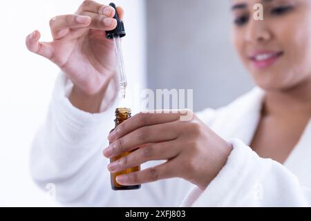 Utilizzando un flacone contagocce, donna in accappatoio che applica siero per la cura della pelle in un ambiente spa Foto Stock
