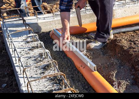 Costruttore edile che misura il livello dei tubi durante la posa e l'installazione di tubi fognari nelle fondamenta di un nuovo edificio Foto Stock