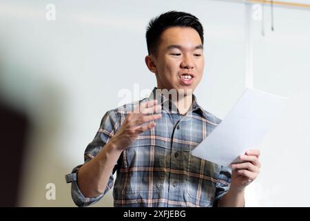 Un giovane studente adolescente sta dando una presentazione davanti alla classe, esercitando le sue abilità di parlare in pubblico. Sta leggendo un giornale scri Foto Stock