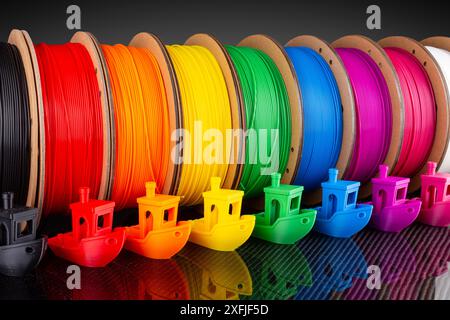 Fila di materiale PLA a filamento per stampa 3d colorato su bobine di cartone riciclabili e ecologiche su backgroun in fibra di carbonio nera Foto Stock