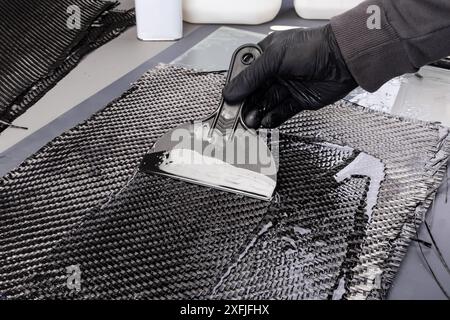 lavorare a mano la resina epossidica in un panno di rinforzo in fibra di carbonio intrecciato. Produzione di un materiale composito CFK laminato a mano. Foto Stock