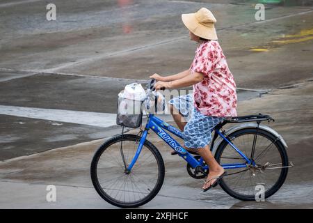 SAMUT PRAKAN, THAILANDIA, 21 MAGGIO 2024, Una donna guida una bicicletta su una strada bagnata Foto Stock