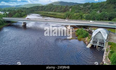 Generatore idroelettrico in acciaio d'argento Hydro Ness sul fiume Ness, Scozia, vista delle ampie colline del fiume e A8082 Holm Mills Bridge Foto Stock