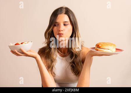 Giovane donna che tiene un'insalata e un hamburger - decisione tra cibo sano e malsano - scelta di dieta, alimentazione sana, concetto nutrizionale, stile di vita cho Foto Stock