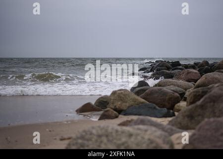 Le onde si infrangono sulla spiaggia rocciosa sotto il cielo coperto al crepuscolo lungo la tranquilla costa Foto Stock