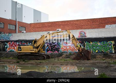 Scavo Komatsu giallo arrugginente, seduto nel mezzo di un cantiere urbano, parzialmente riflesso da una pozza d'acqua in primo piano Foto Stock