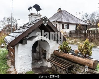 Un forno in mattoni del XIX secolo a Lenora, Sumava, Cechia. Con una struttura dipinta di bianco, tetto in legno e apertura ad arco. Circondato da alberi e case rurali. Foto Stock