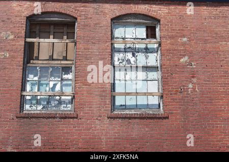 Edificio industriale in mattoni abbandonato con finestre rotte e usurate dalle intemperie Foto Stock