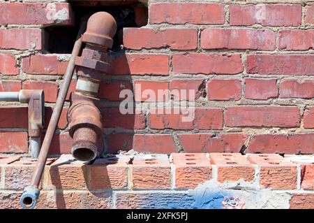 Condotto e tubi metallici che escono da una parete di mattoni Foto Stock