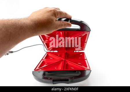 Una persona ha in mano un forno con tostapane rosso e nero. Il forno con tostapane è aperto e pronto per l'uso Foto Stock