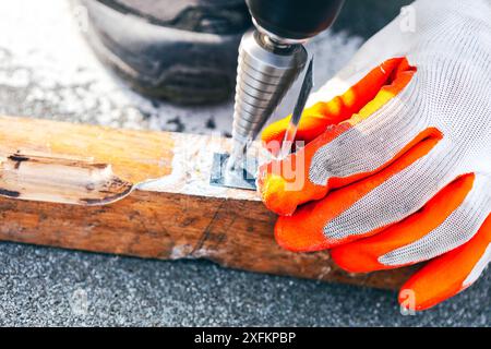 L'uomo sta usando un trapano per realizzare un foro in un pannello di legno. Indossa guanti arancioni per lavoro Foto Stock