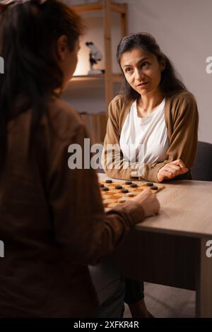 Due donne impegnate in intense Checkers Game at Home, attività di svago da tavolo Foto Stock