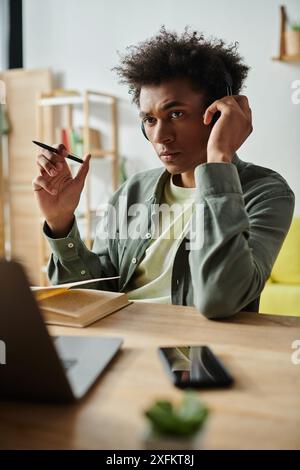 Un giovane di origini afroamericane si concentra sul suo laptop e indossa le cuffie mentre studia a una scrivania. Foto Stock