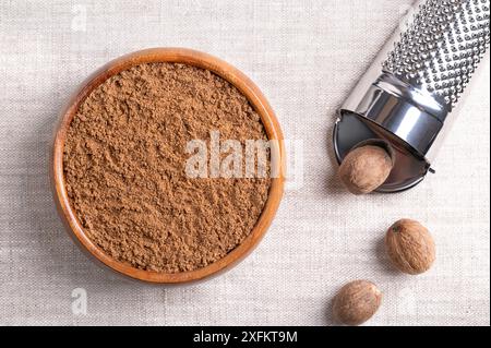 Noce moscata in polvere, noce moscata macinata in un recipiente di legno su tessuto di lino. Fragrante o vera noce moscata, una spezia, utilizzata anche nella medicina tradizionale. Foto Stock