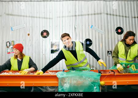 I giovani volontari che indossano guanti e giubbotti di sicurezza collaborano per smistare i rifiuti su un tavolo. Foto Stock