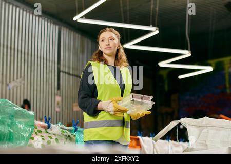 Una giovane volontaria in un gilet giallo che tiene una ciotola di cibo, che mostra i suoi sforzi eco-consapevoli nella selezione dei rifiuti. Foto Stock