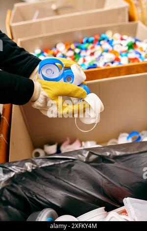 Un giovane volontario in guanti e giubbotto di sicurezza che tiene in mano la plastica durante lo smistamento dei rifiuti, mantenendo la consapevolezza dell'ambiente. Foto Stock