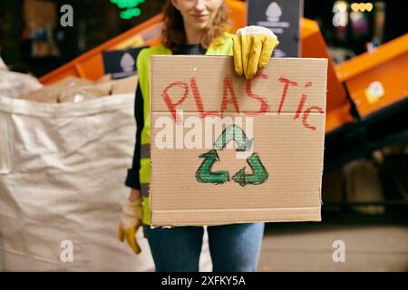 Un giovane volontario in guanti e un giubbotto di sicurezza con un cartello di cartone che dice plastica durante la selezione dei rifiuti. Foto Stock