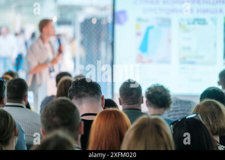 Relatore che offre una presentazione a un vasto pubblico durante una conferenza o un seminario, con i partecipanti che ascoltano attentamente. Foto Stock